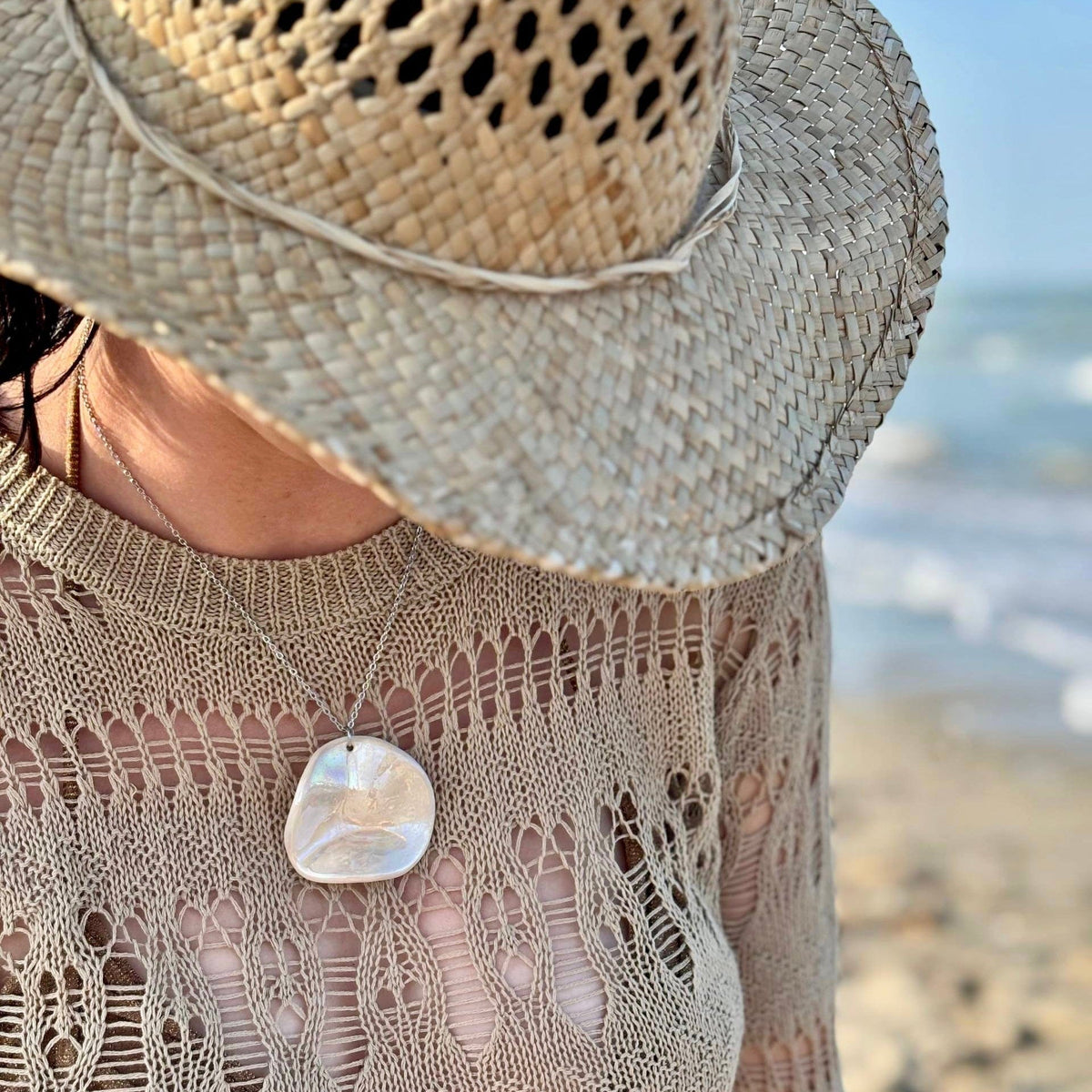 Mujer con the pearl-white ceramic pendant necklace at the beach with a wide straw hat.