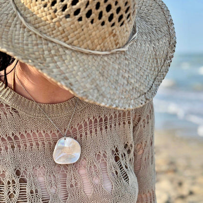 Mujer con the pearl-white ceramic pendant necklace at the beach with a wide straw hat.