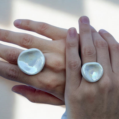 Close-up of two hands wearing oversized pearl white ceramic rings from the Perla collection.