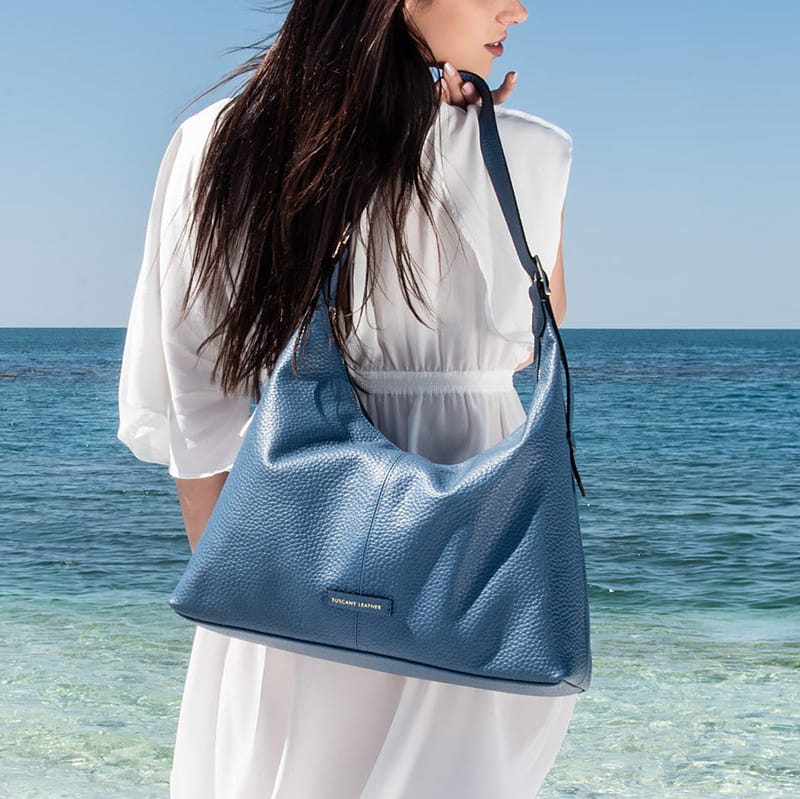 Mujer sosteniendo un bolso azul junto al océano