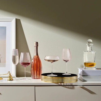 Dusty rose tinted wine glasses on a white surface with a champagne bottle and decanter