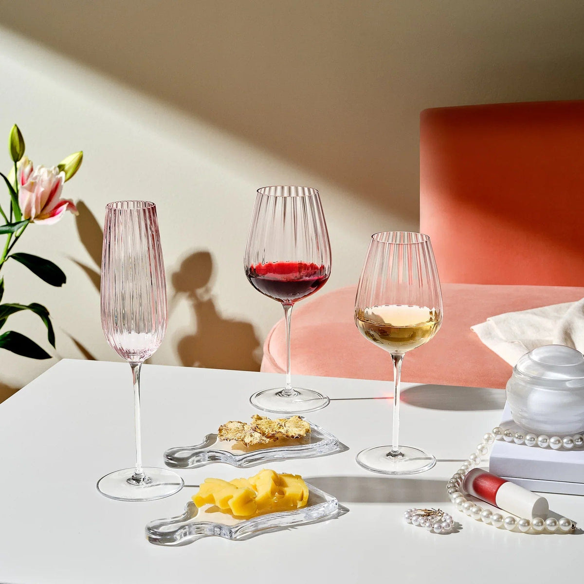 Three ribbed wine glasses in pink and clear tones on a white table with cheese and decor