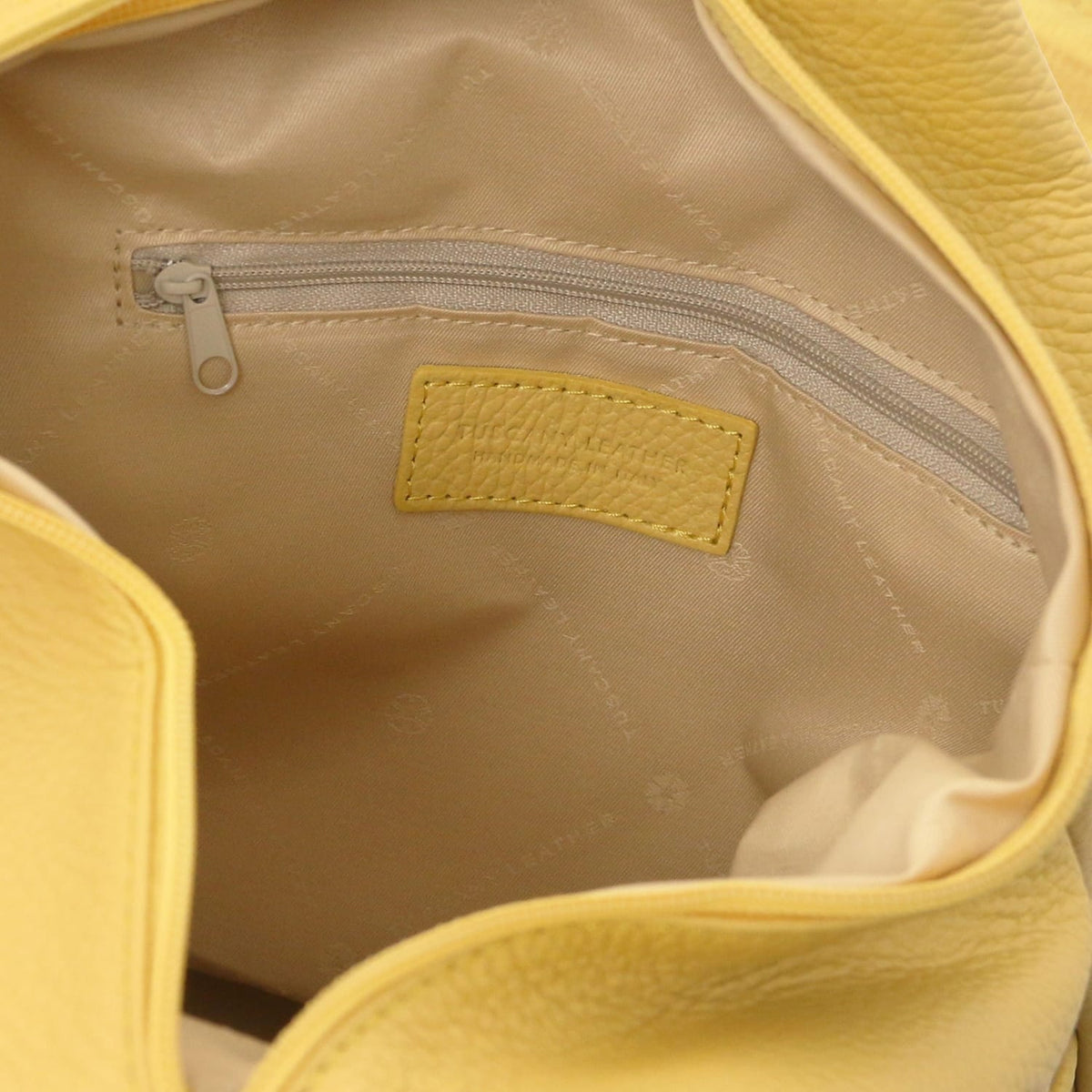 Interior of yellow Italian leather backpack showing a tasca con zip e a yellow stitched bre patch on fodera beige.