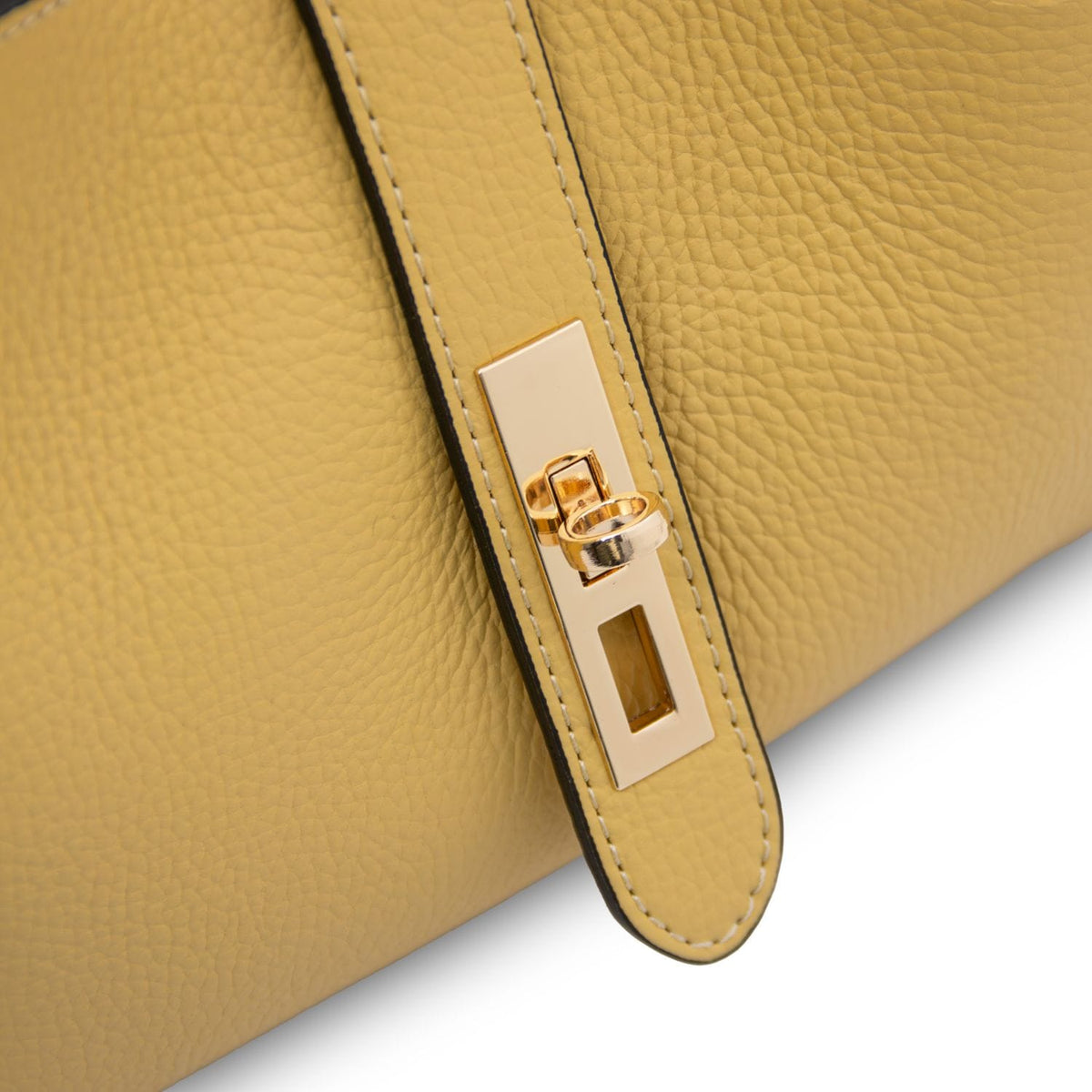 Edge detail of mustard yellow leather bag with gold rectangular plate and ring hardware.