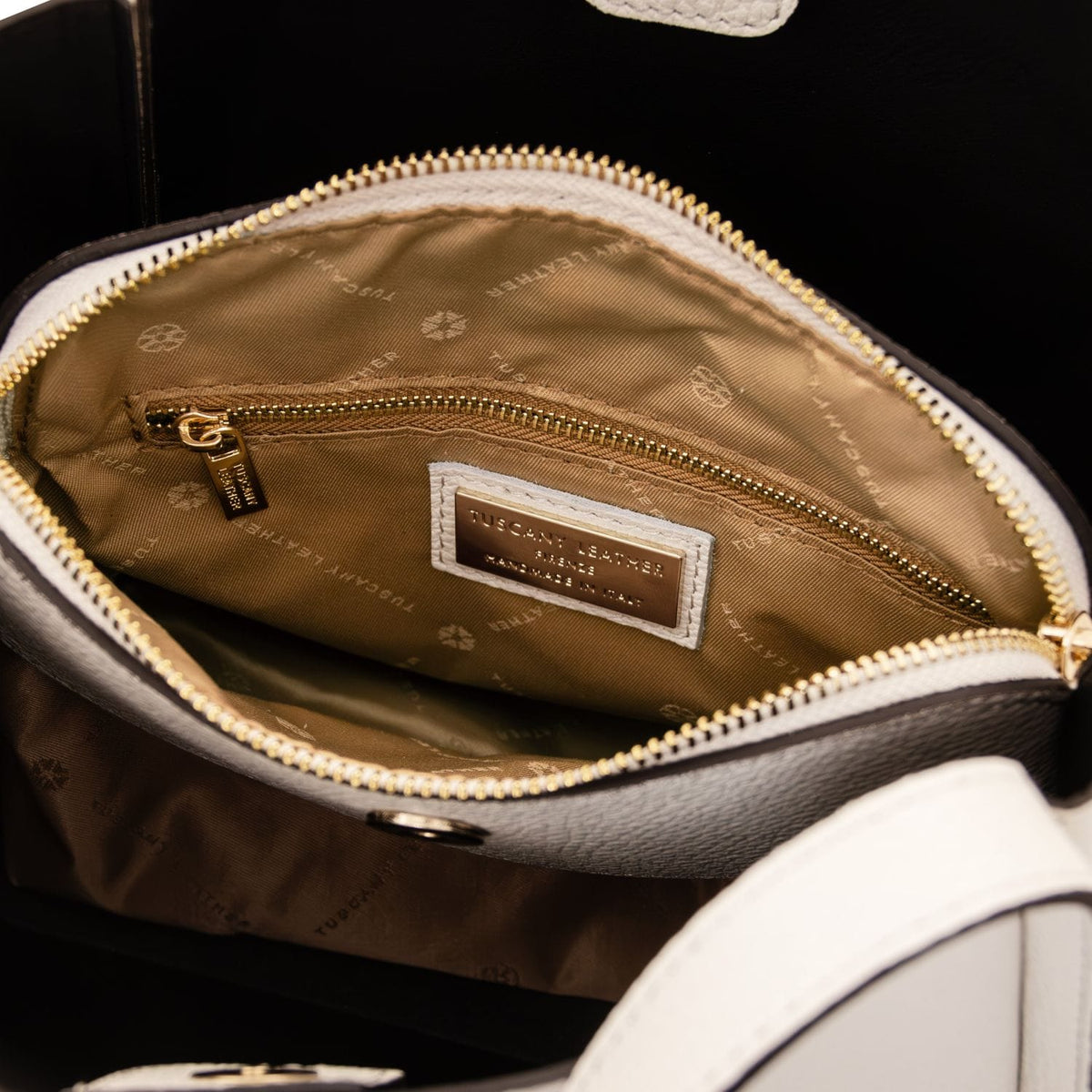 Interior view of beige handbag with tan lining gold zip pocket and brand label.