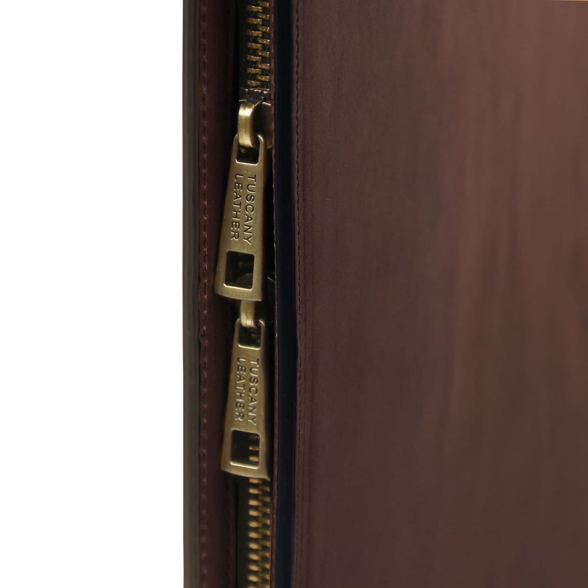 Primer plano of brass zipper on brown leather document case with Tuscany Leather engravings.