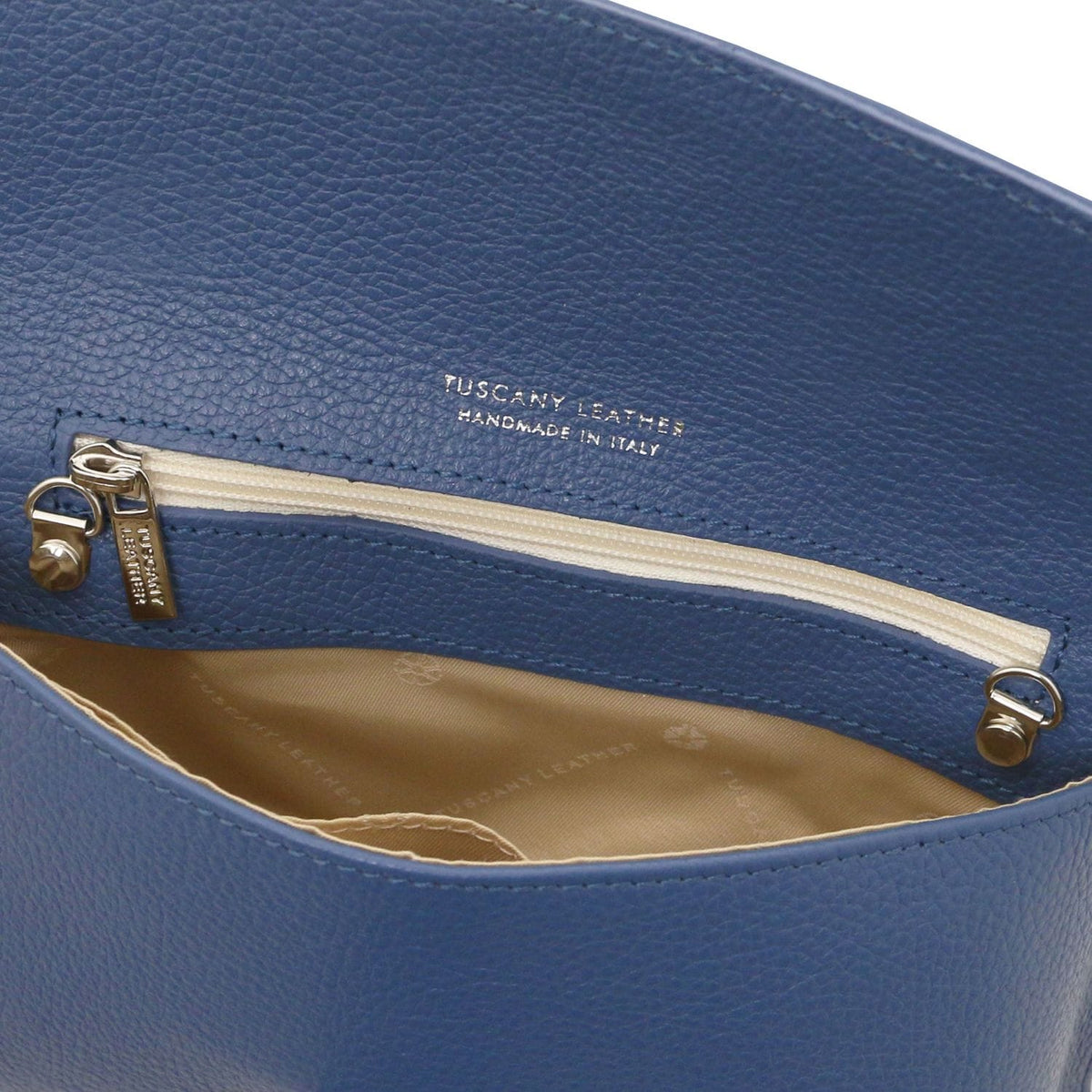 Gros plan of blue leather clutch montrant inner poche zippée with doublure beige and tirette dorée.