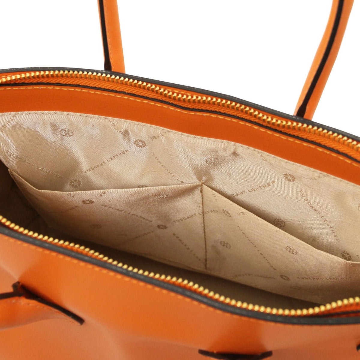 Primer plano of an orange leather handbag interior showing beige forro de tela with printed logo pattern and zippered opening.