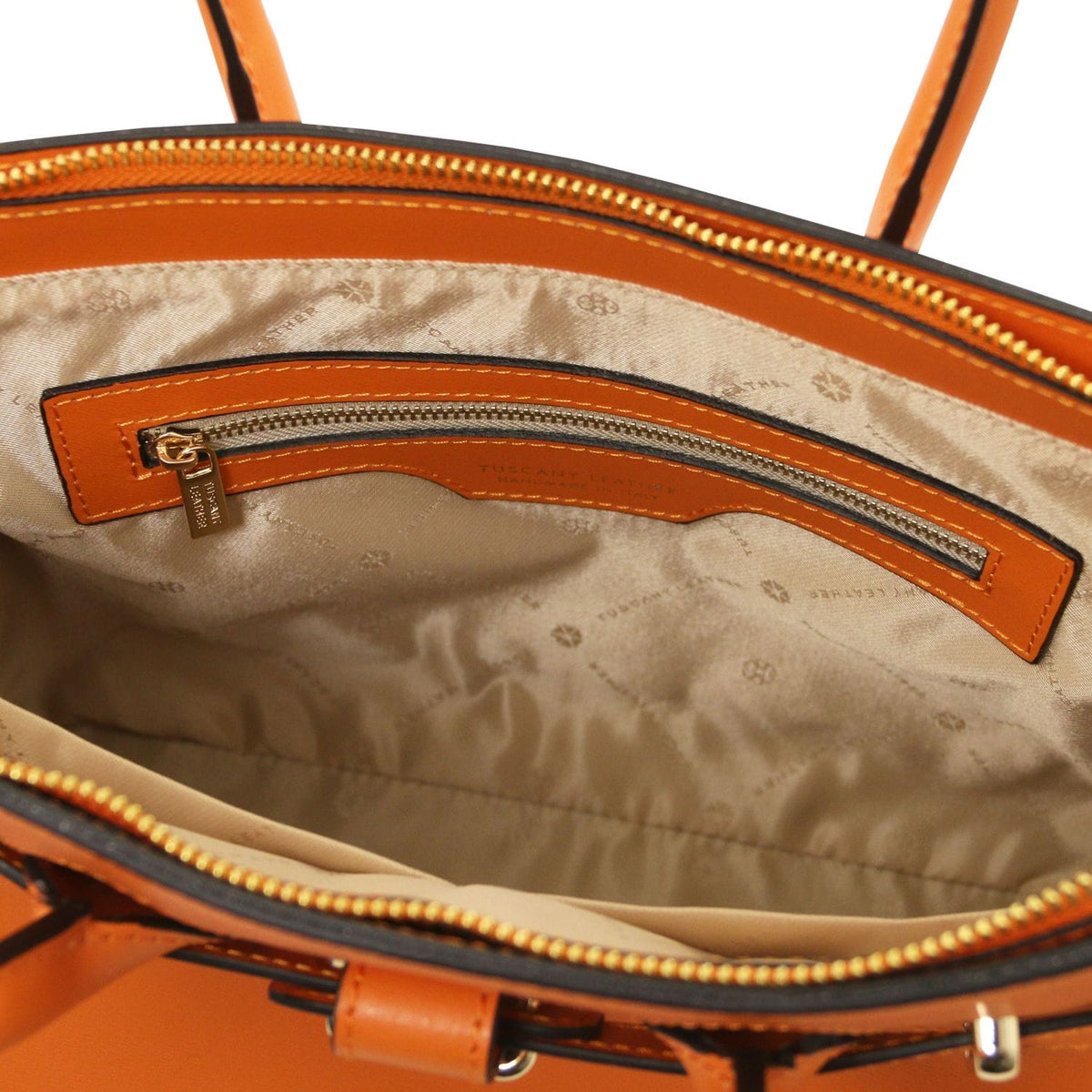 Vista interior of orange leather handbag with beige patterned lining and an inner bolsillo con cremallera with gold-tone zipper pull.
