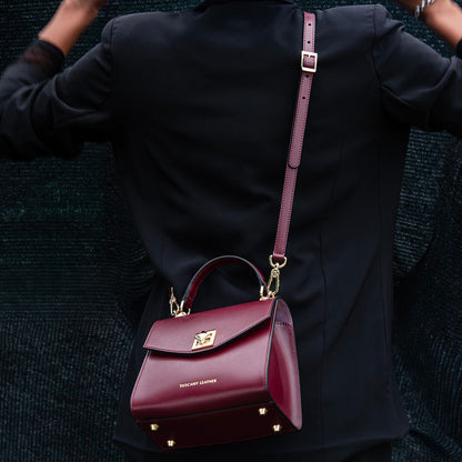 burgundy leather TL Bag mini bag with gold hardware and a long strap worn over a black coat