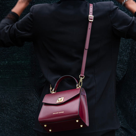 burgundy leather TL Bag mini bag with gold hardware and a long strap worn over a black coat