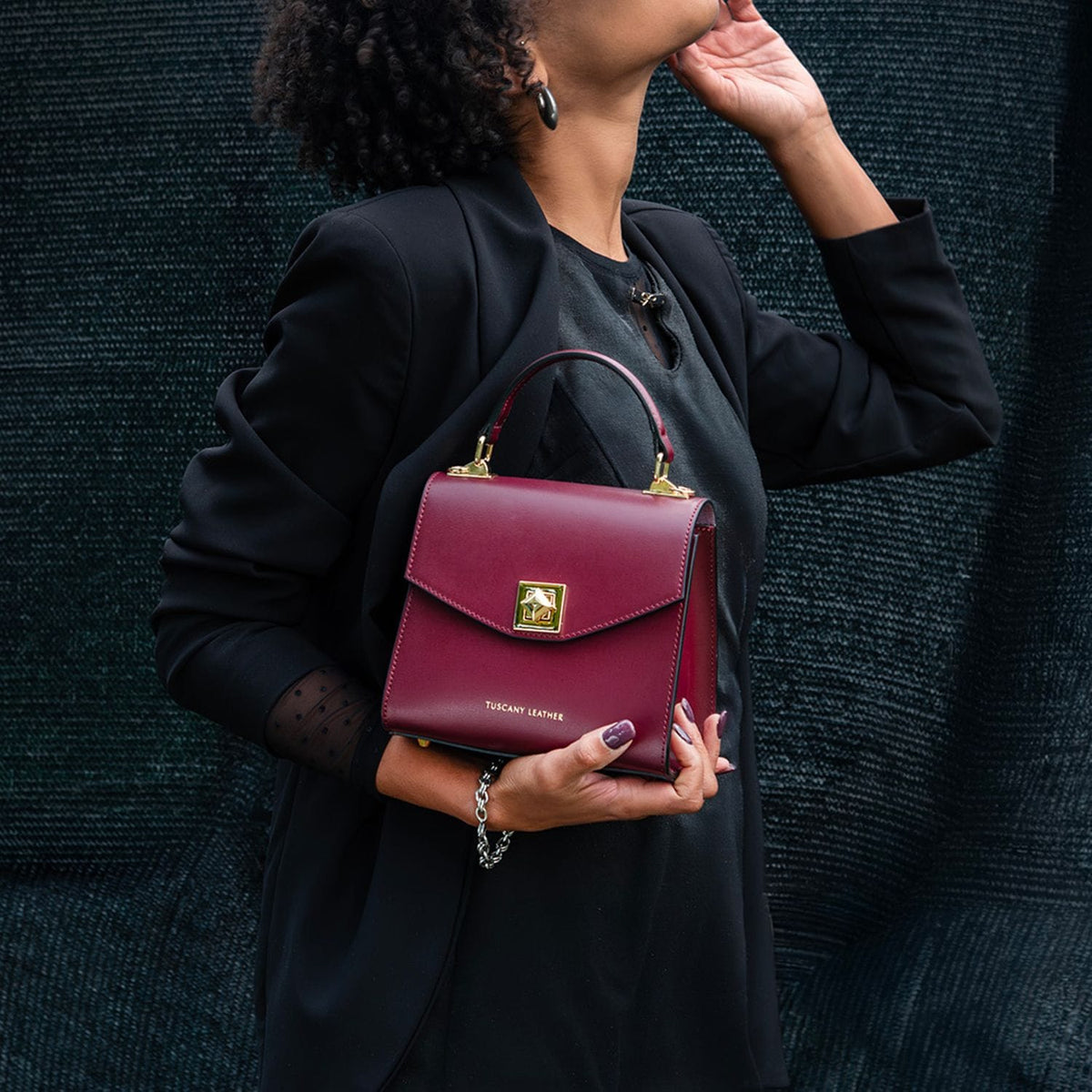 Burgundy leather TL Bag mini handbag with a gold square clasp and top handle, held by a person in a black blazer.