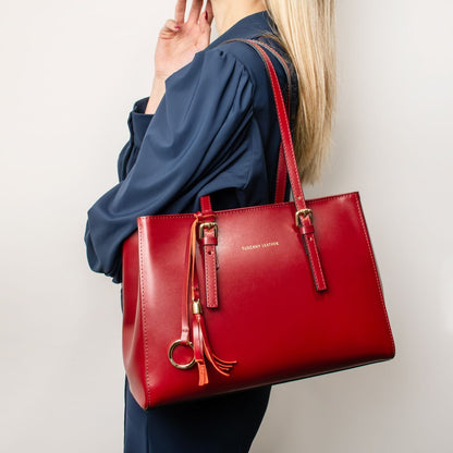 Vibrant red leather tote with gold hardware and tassel carried by a model in a navy blouse