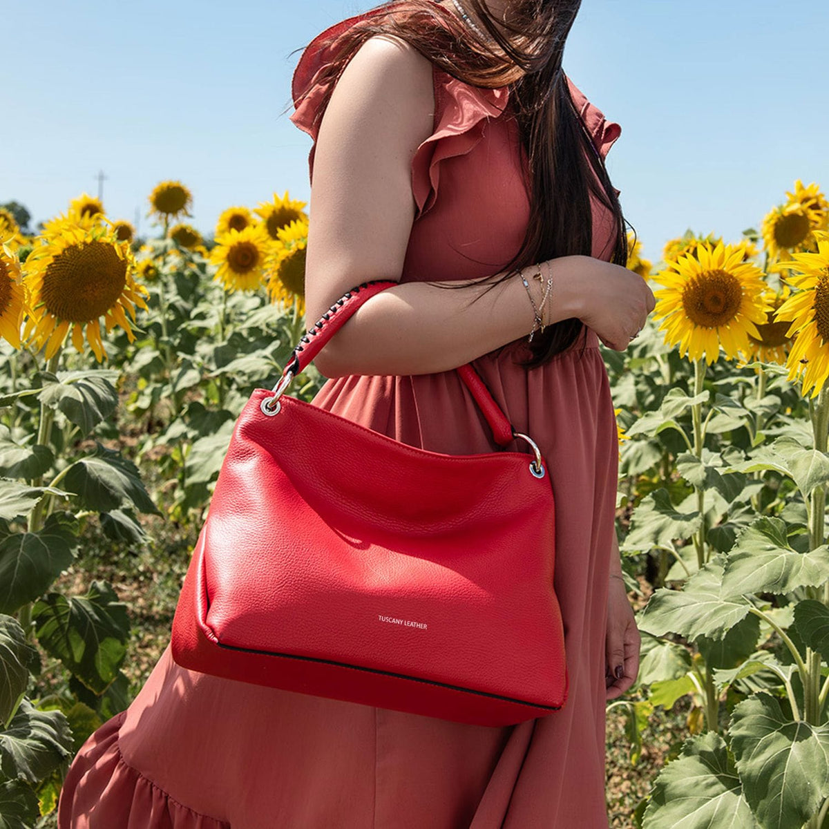 Rosso soft borsa a spalla in pelle italiana con silver ring hardware carried by a woman in a sunflower field.