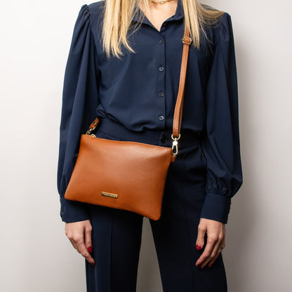 Tan pebbled leather TL Bag pouch clutch with a brown adjustable strap worn crossbody over a navy outfit.