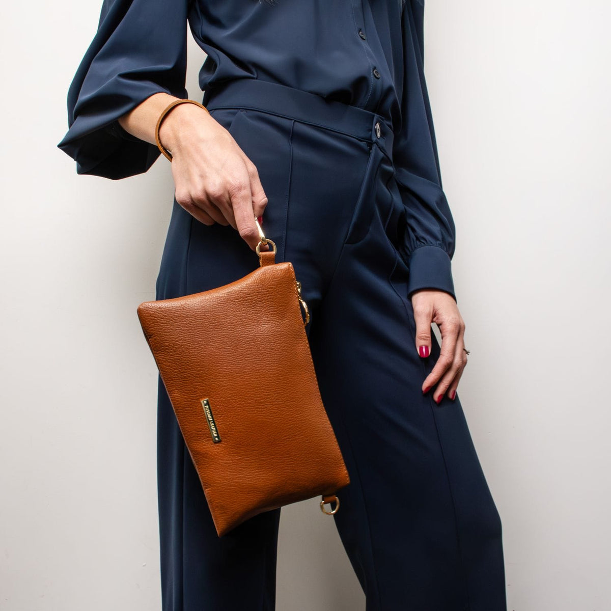 Tan pebbled leather pouch clutch held by a model wearing a navy blue tailored outfit.
