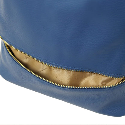 Gros plan of blue leather TL Bag backpack exterior with a fermeture zippée dorée along a curved opening.