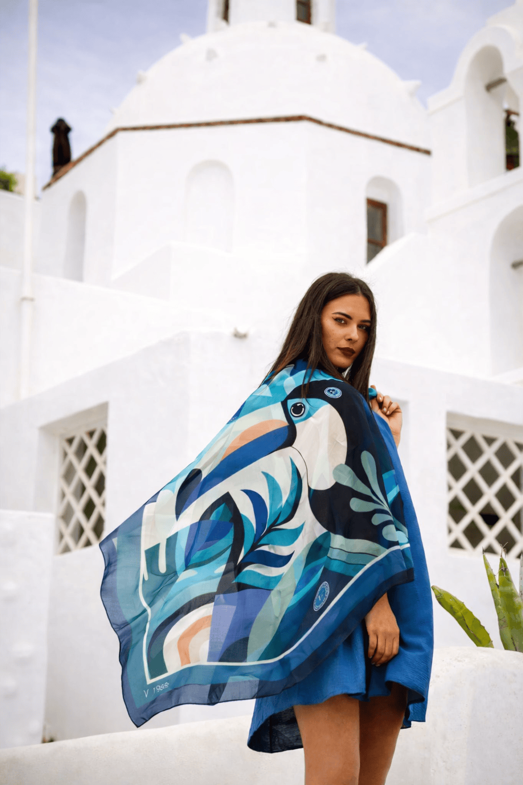 Woman holding a colorful toucan silk scarf in front of a white building