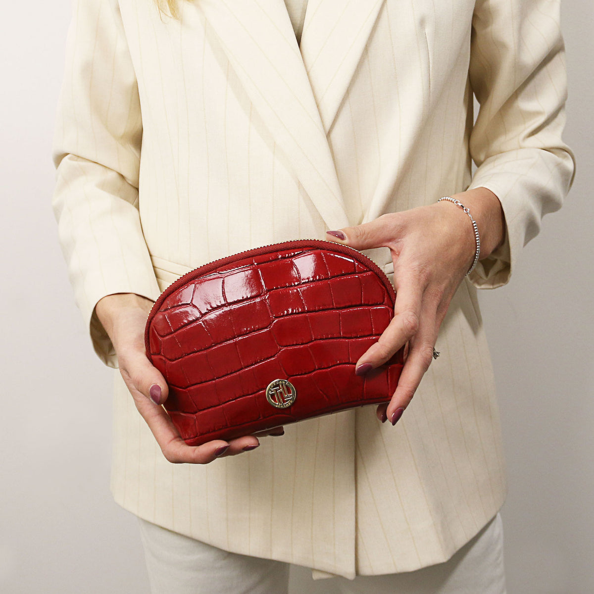 Vera - Croc print leather toiletry case | TL142514 in deep red with embossed leather, gold-tone hardware, and zip closure held by person in cream blazer.