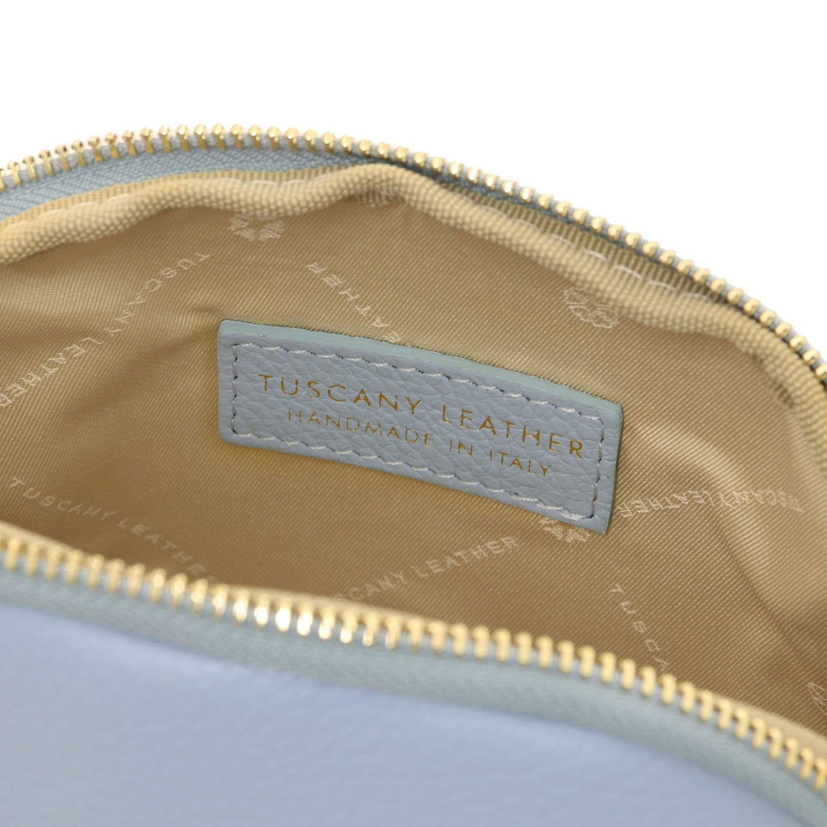 Primer plano of a piel suave toiletry case interior showcasing beige forro de tela and stitched Tuscany Leather label inside zipper closure.