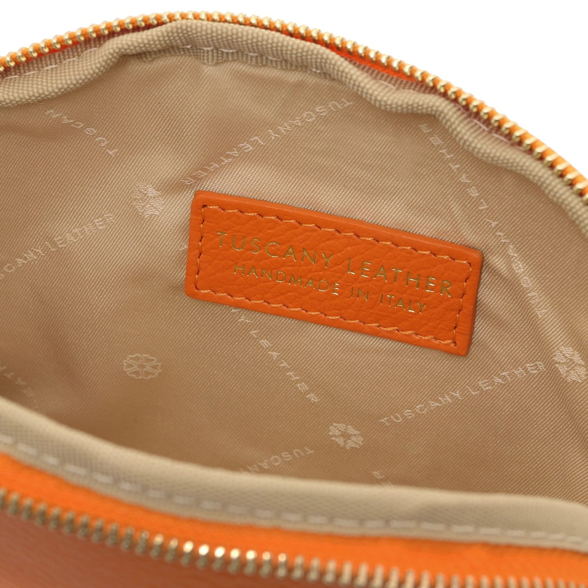 Primer plano of beige fabric forro interior with embossed Tuscany Leather branding and stitched orange leather label inside toiletry case.