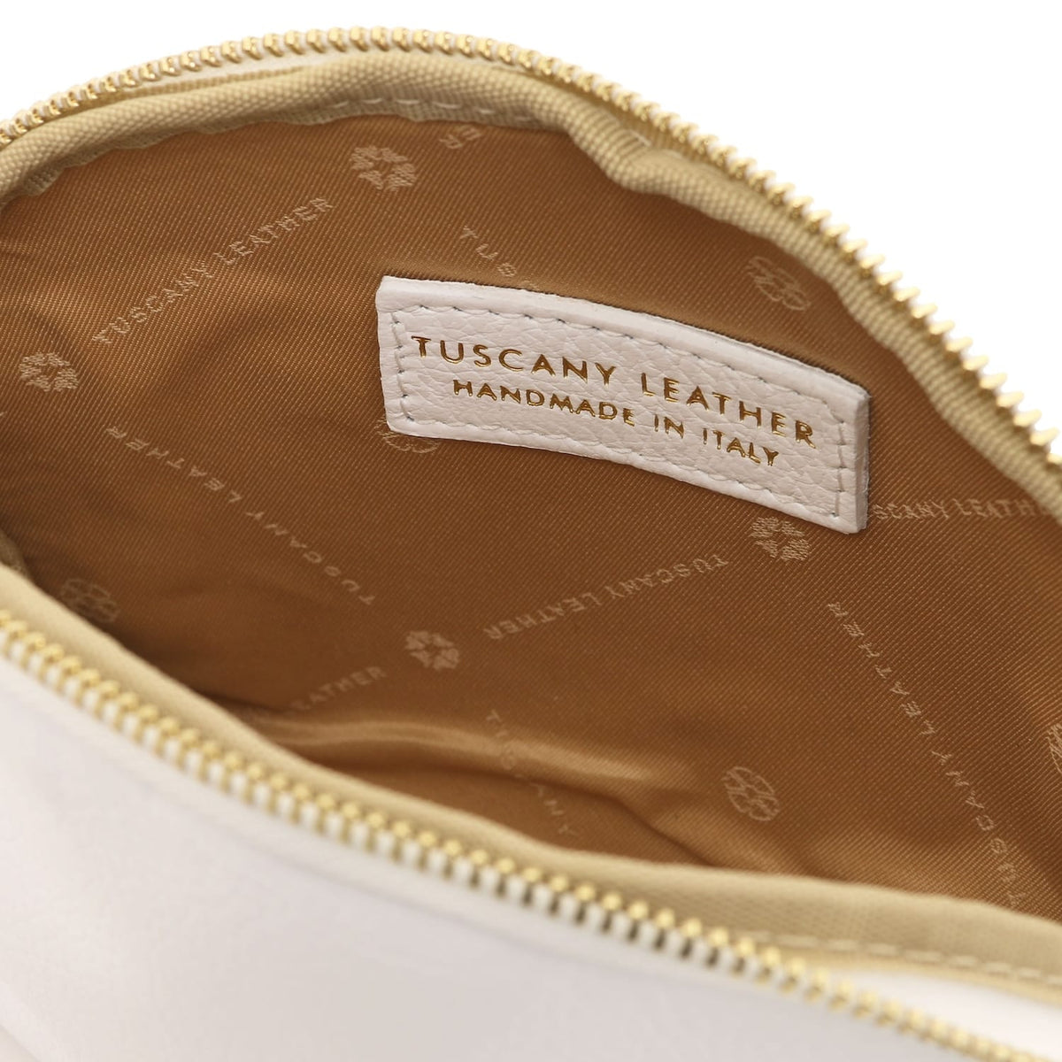 Primer plano of beige leather toiletry case interior featuring branded forro de tela and stitched Tuscany Leather label inside zipper opening.