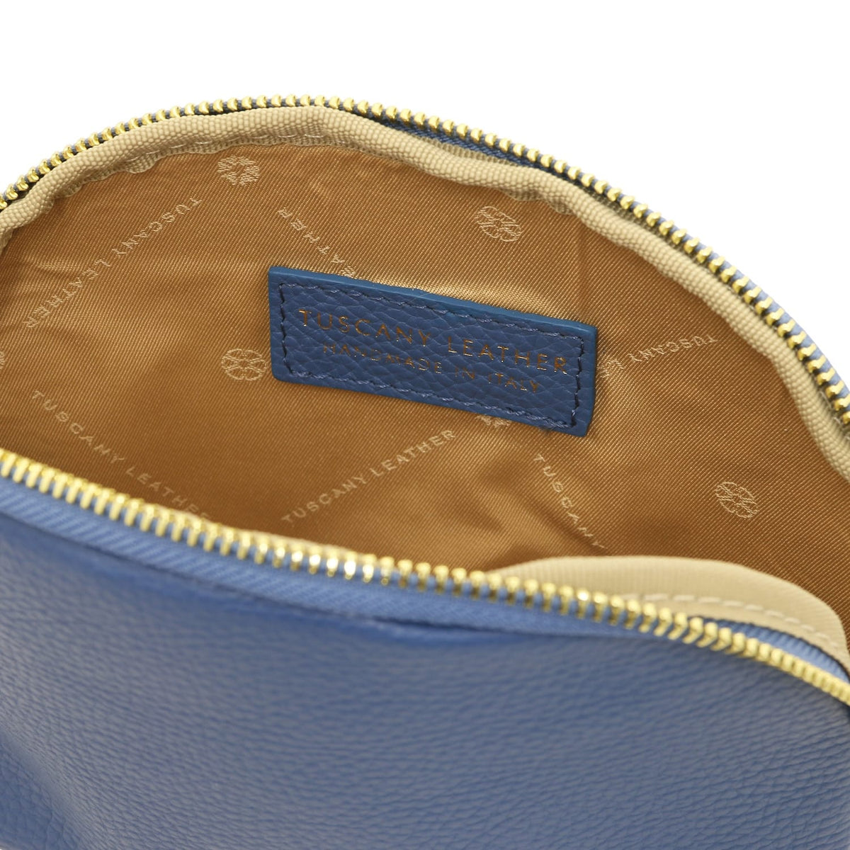 Primer plano of blue leather toiletry case interior showing beige forro de tela and embossed Tuscany Leather made in Italy label.